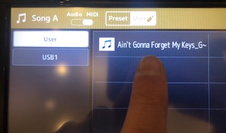 An image of a Genos digital display with a specific song file highlighted.