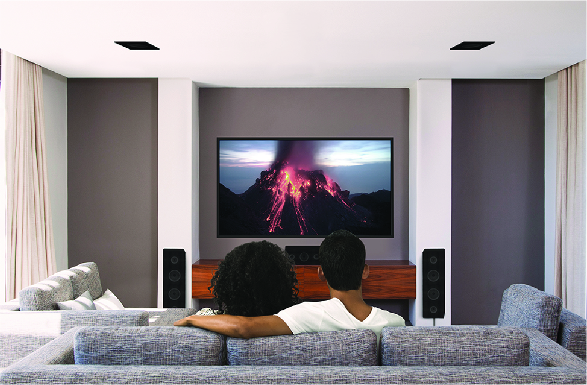 A couple sits on a couch and watches television with a surround sound system.