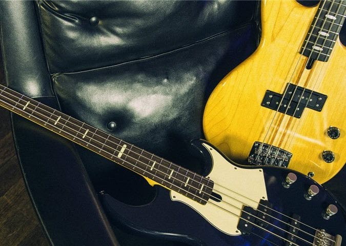 Two electric bass guitars on a leather arm chair.