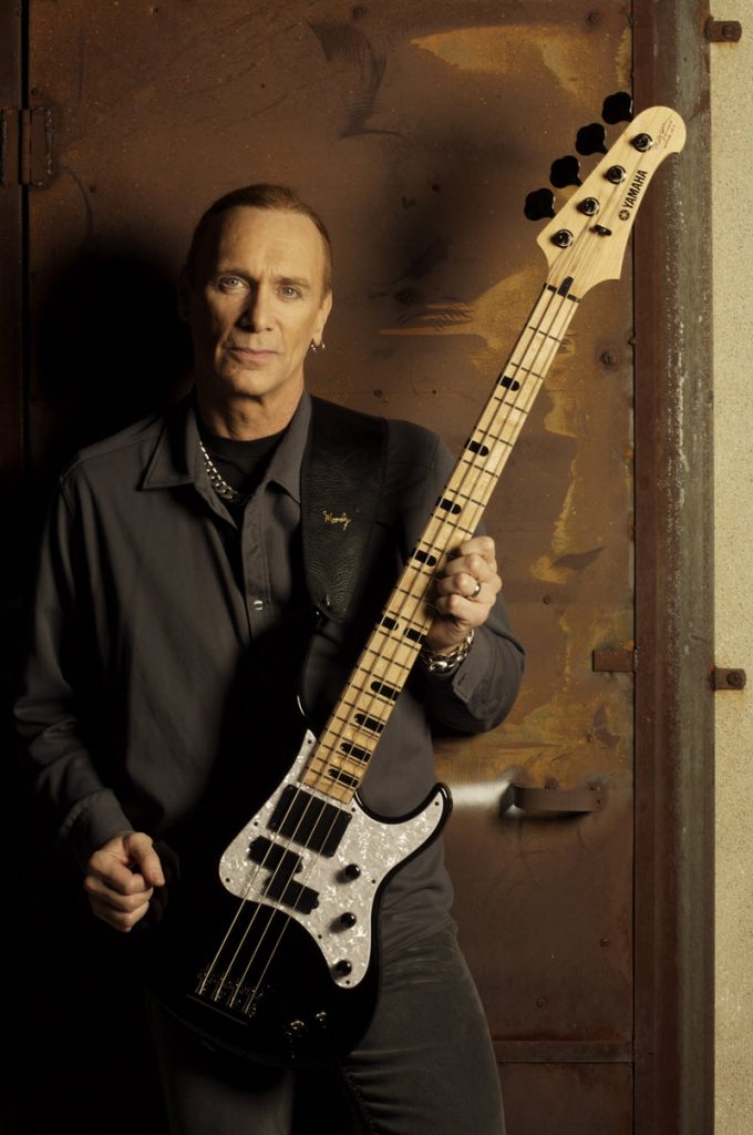 Tall slim man in his 40's holding a bass guitar.