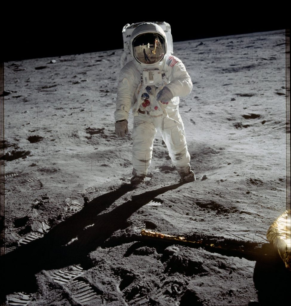 Person in space suit and helmet standing on sanding desolate surface.