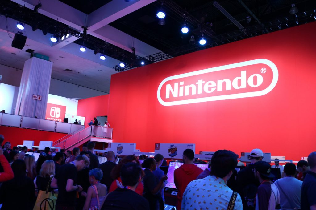 Dense crowd clustered in front of a large tradeshow booth with an enormous Nintendo logo on wall in background.