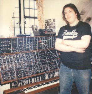 Young man standing to the side of a large synthesizer.