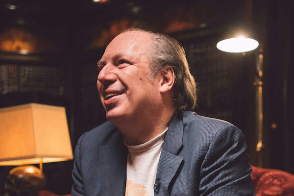 Hans Zimmer smiling genuinely in warmly-lit studio.