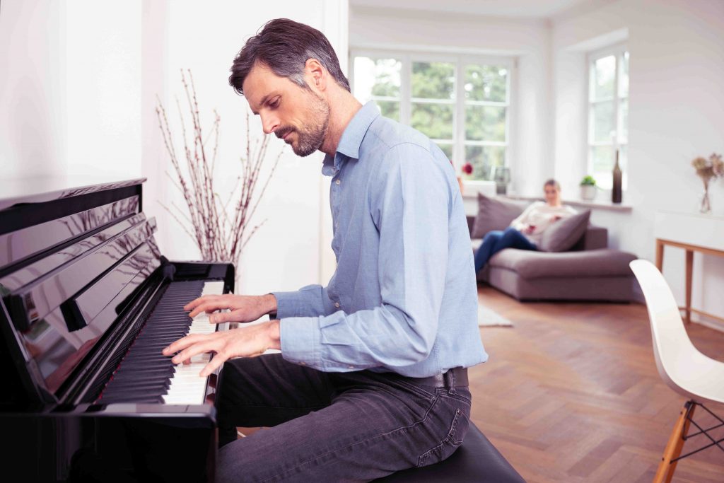 Man playing spinet piano in living room.