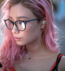 Young woman with pink hair and black rimmed glasses wearing Yamaha TW-E3A earbuds.