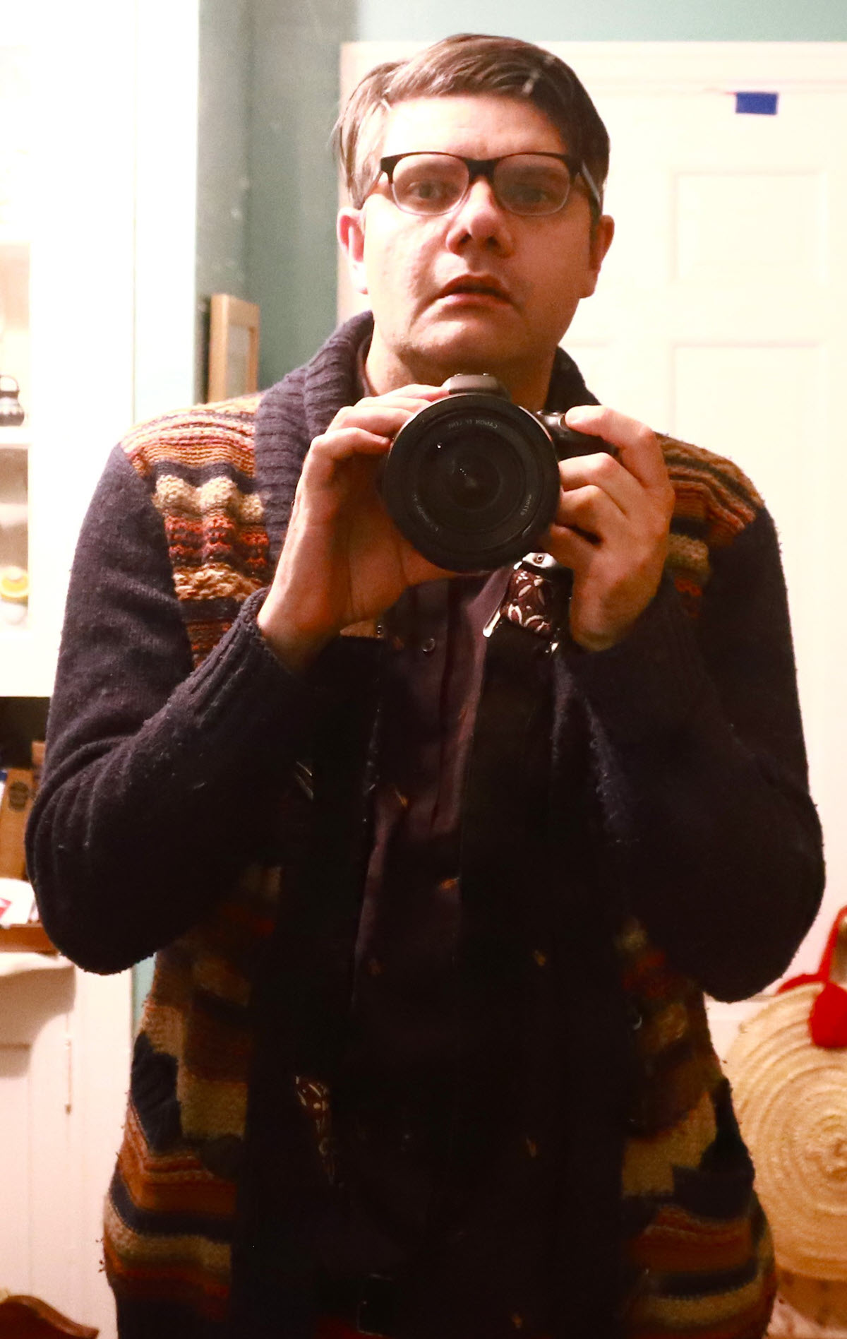 Man in glasses holding a camera. Appears to be taking this picture of himself via a mirror.