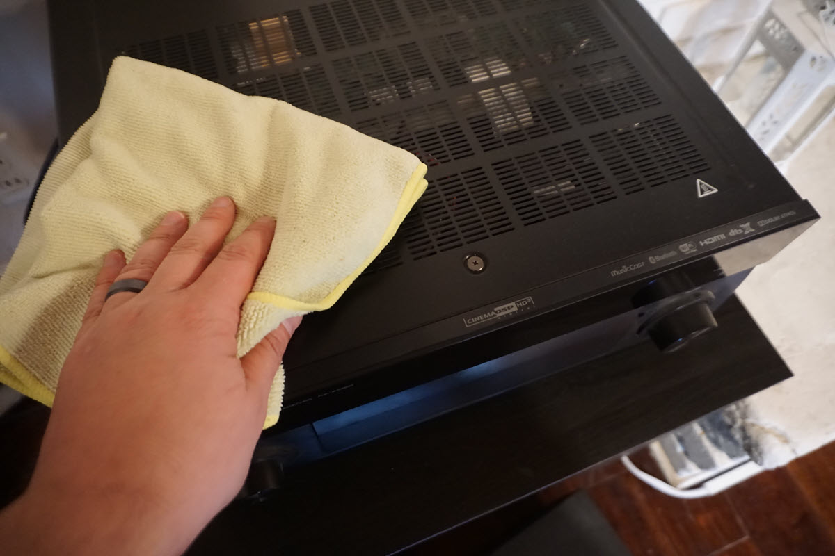 Closeup showing someone's hand with a soft cloth cleaning the vents on a piece of audio equipment.