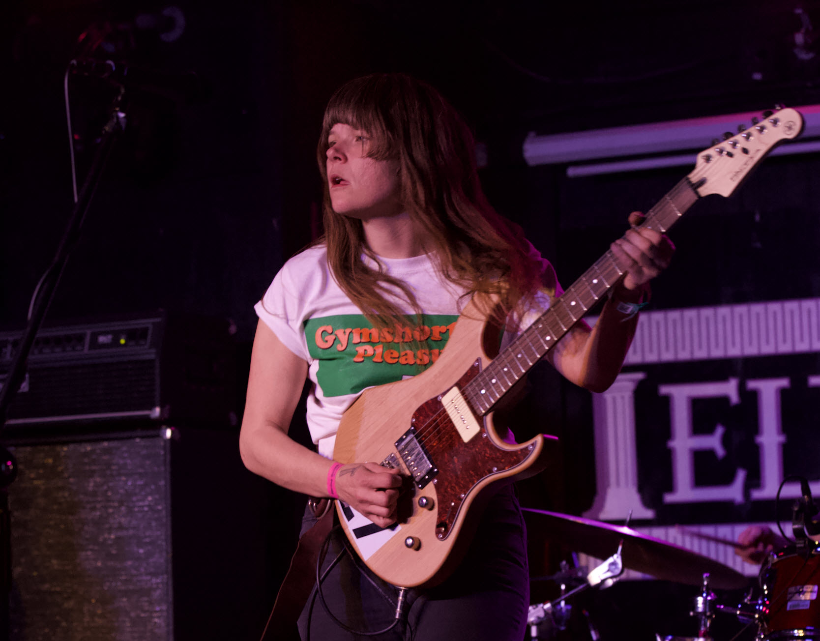 Woman with long hair and a t-shirt rocking out on a guitar on stage.