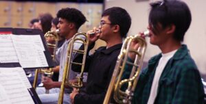 trombone section holding mouth pieces to their face 
