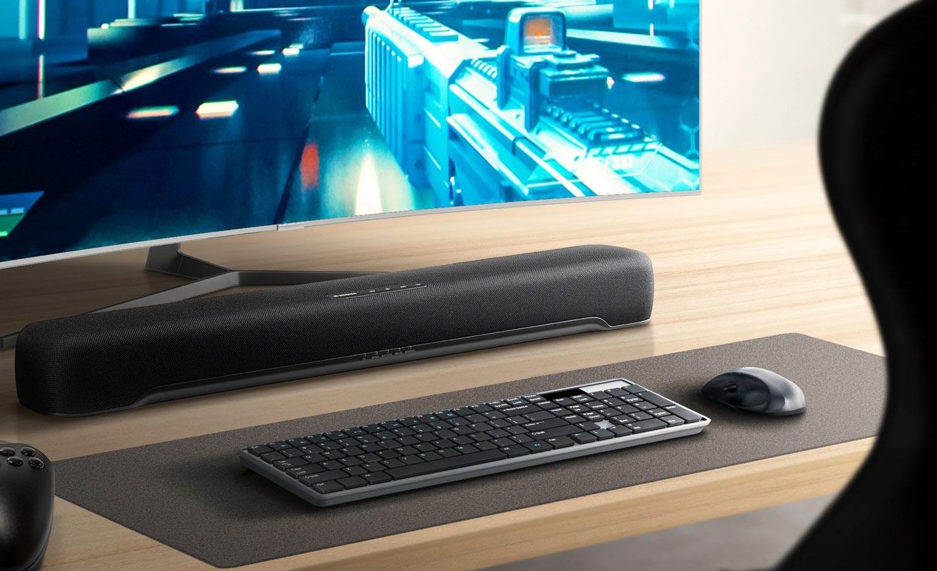 Soundbar on desk between the keyboard and the large curved screen of a gaming system.
