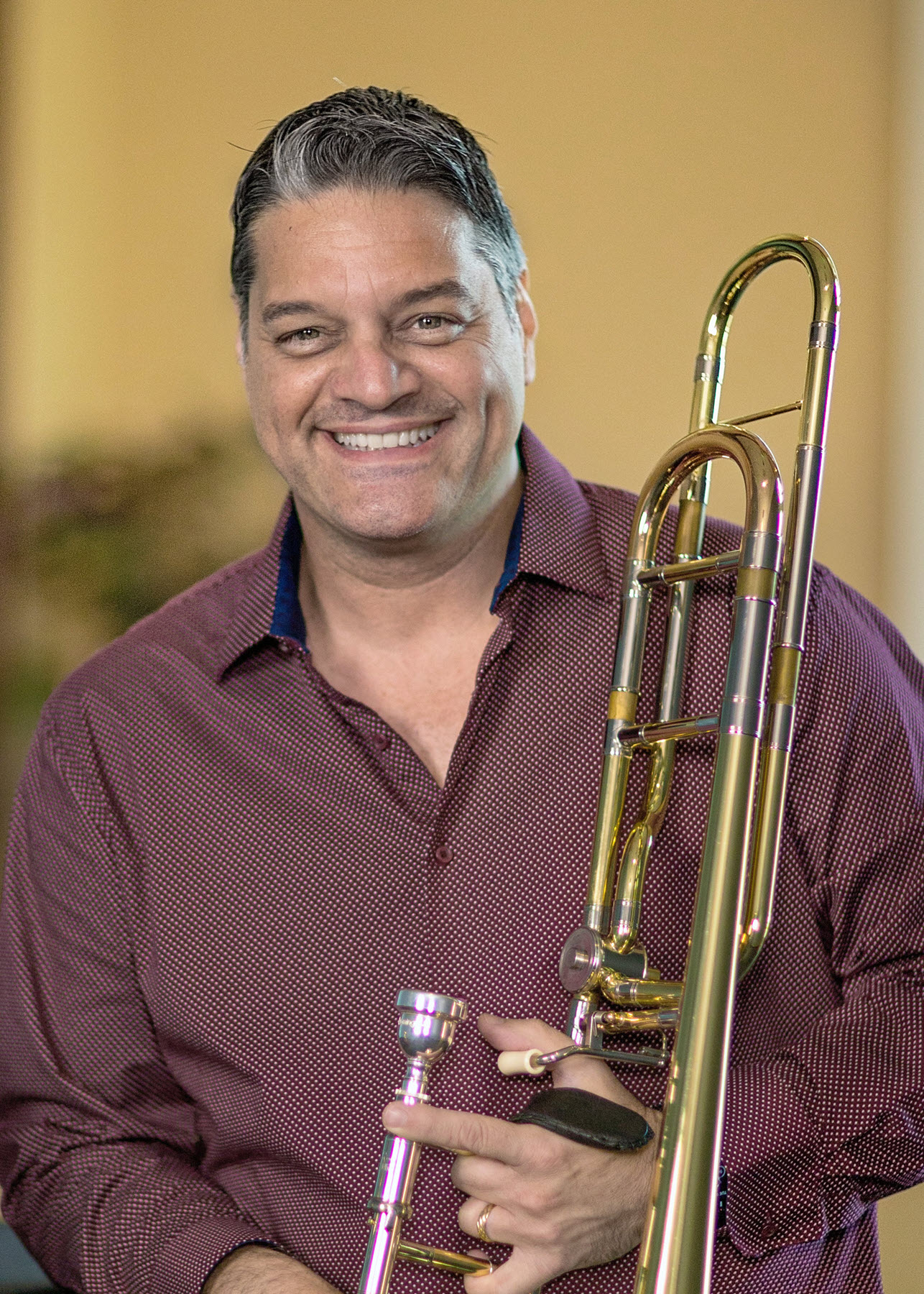 Headshot of smiling man holding a trombone.