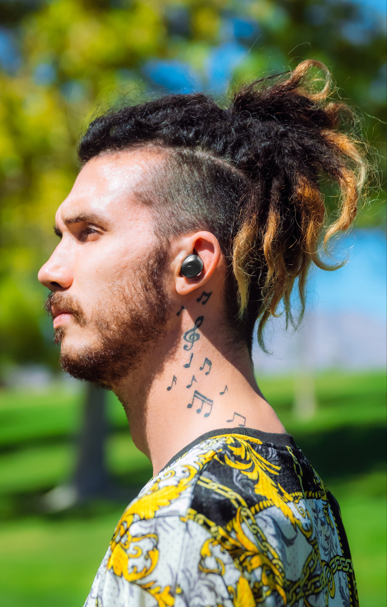 Young man with dreads and body art wearing earbuds. Seen in profile.