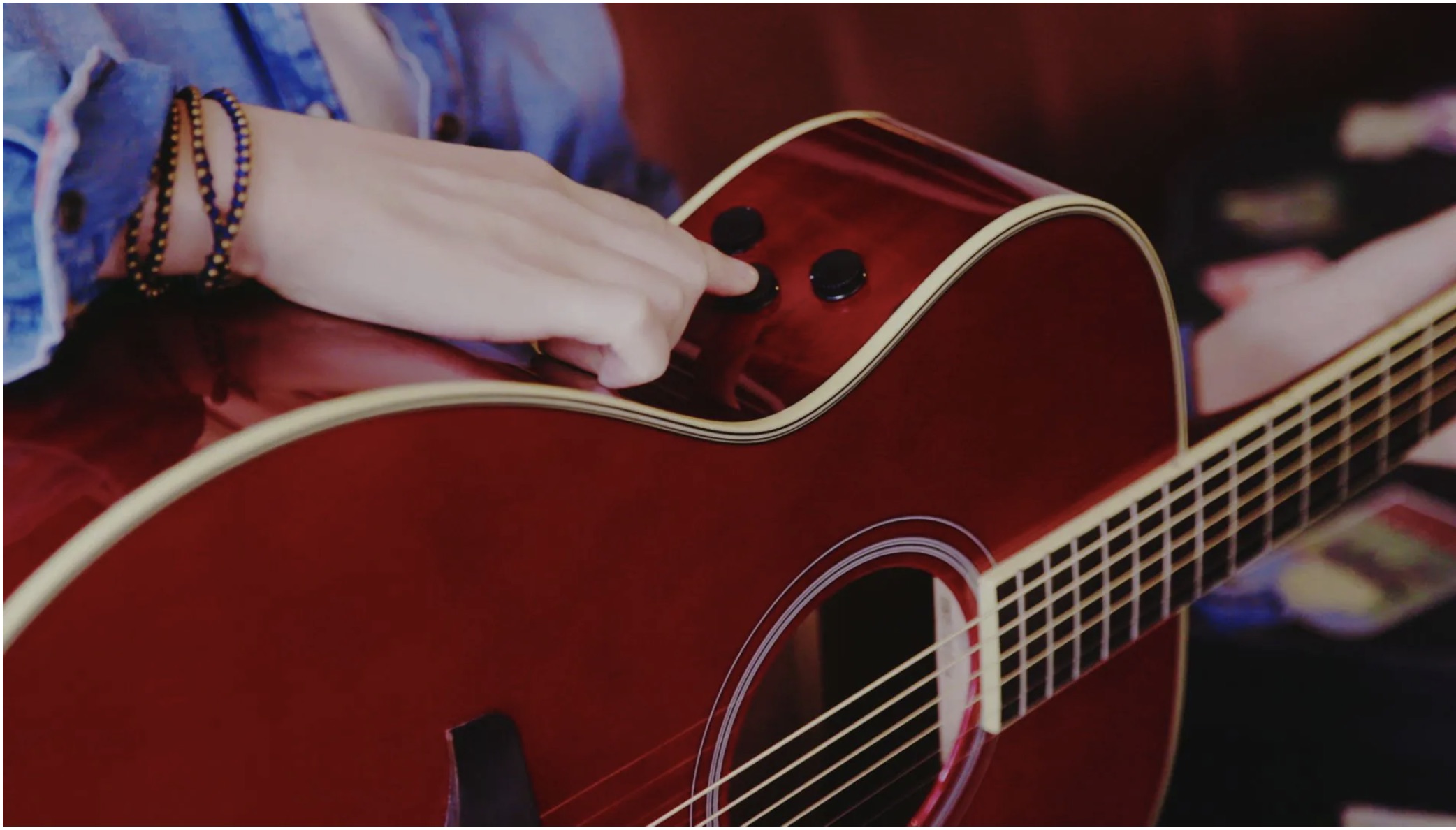 Closeup of author's hand pointing out the knobs on the side of the acoustic guitar.