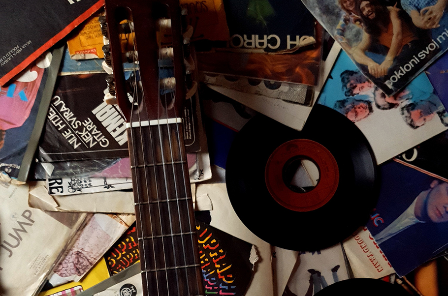 A messy collection of album covers, a 45 record and an acoustic guitar.