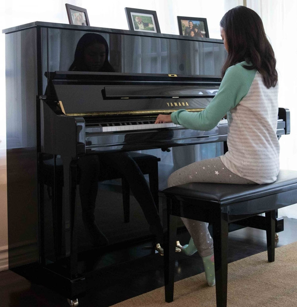 Young child playing an upright piano in her living room.