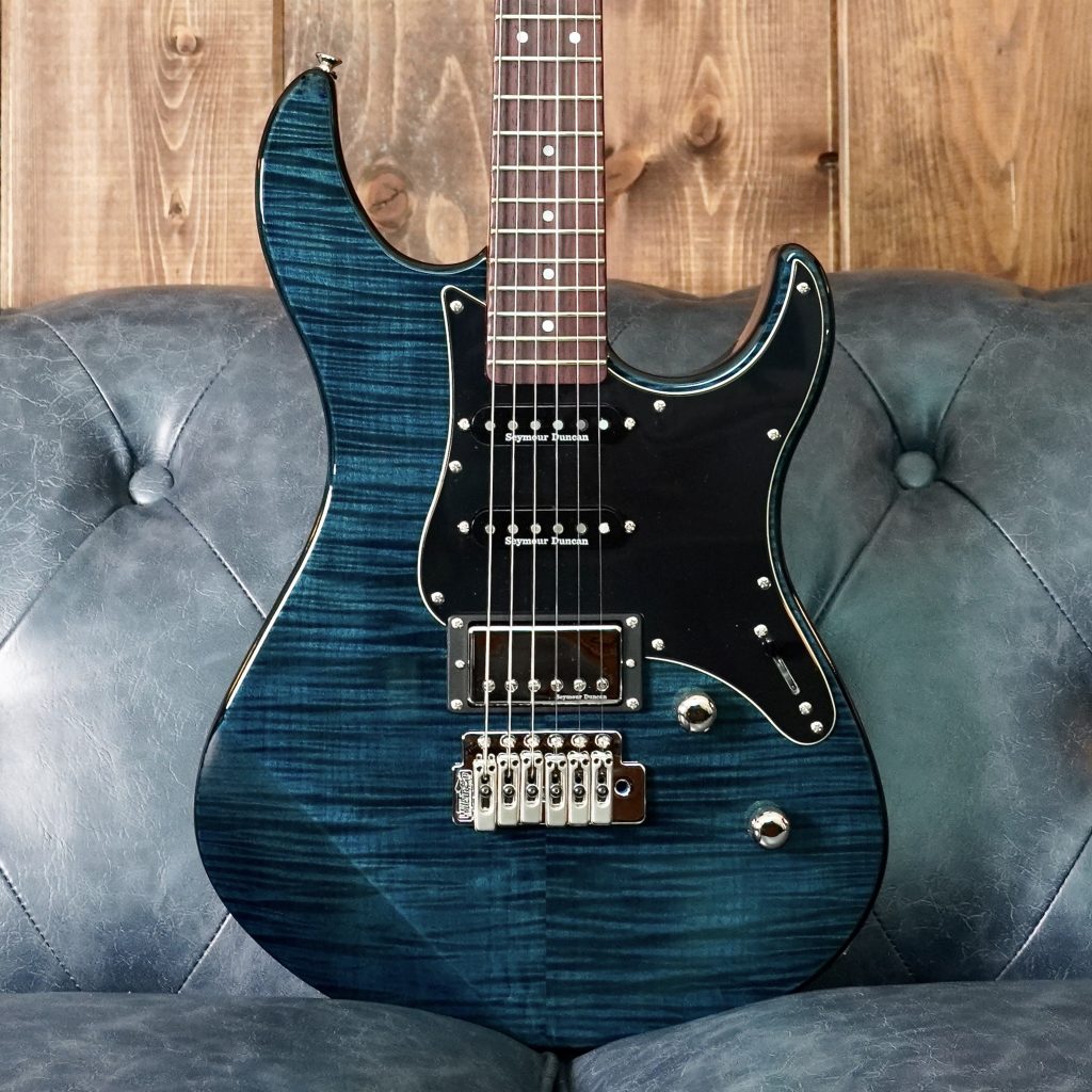Beautiful blue electric guitar standing on a blue couch with a wood wall in background.