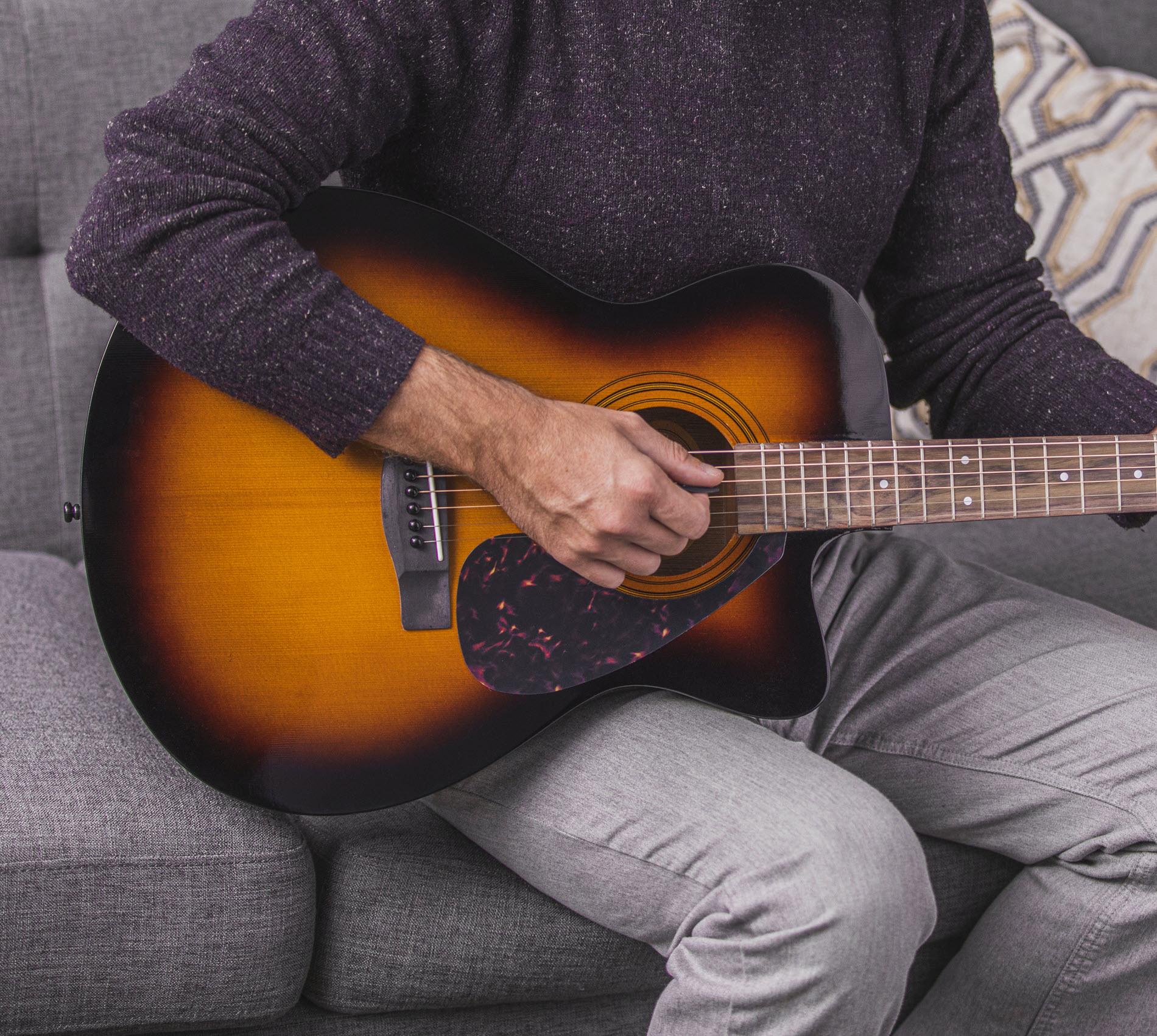 Closeup of someone seated on a couch playing an acoustic guitar.