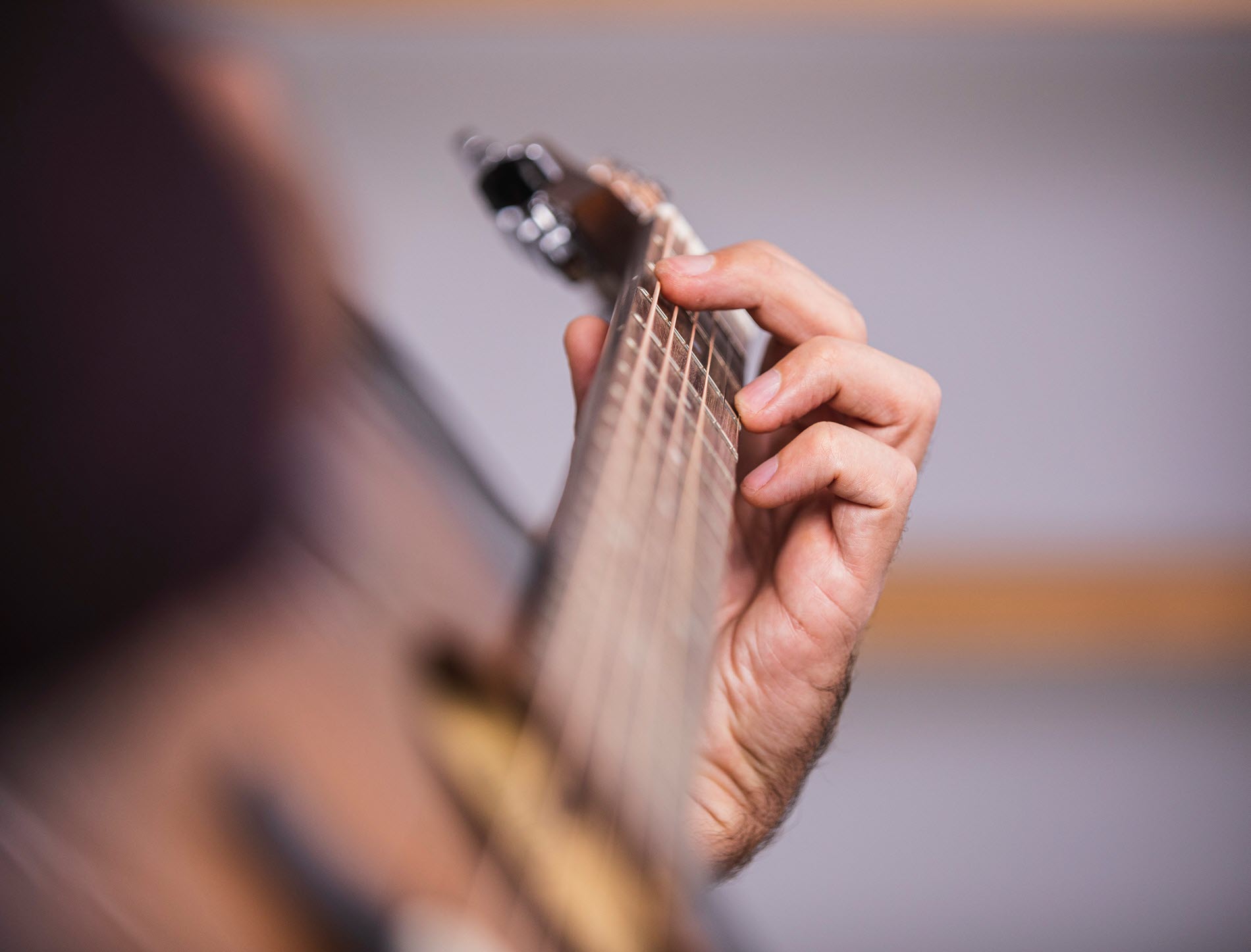 Closeup from side angle of someone playing an acoustic guitar with focus on hand placement on neck of guitar.