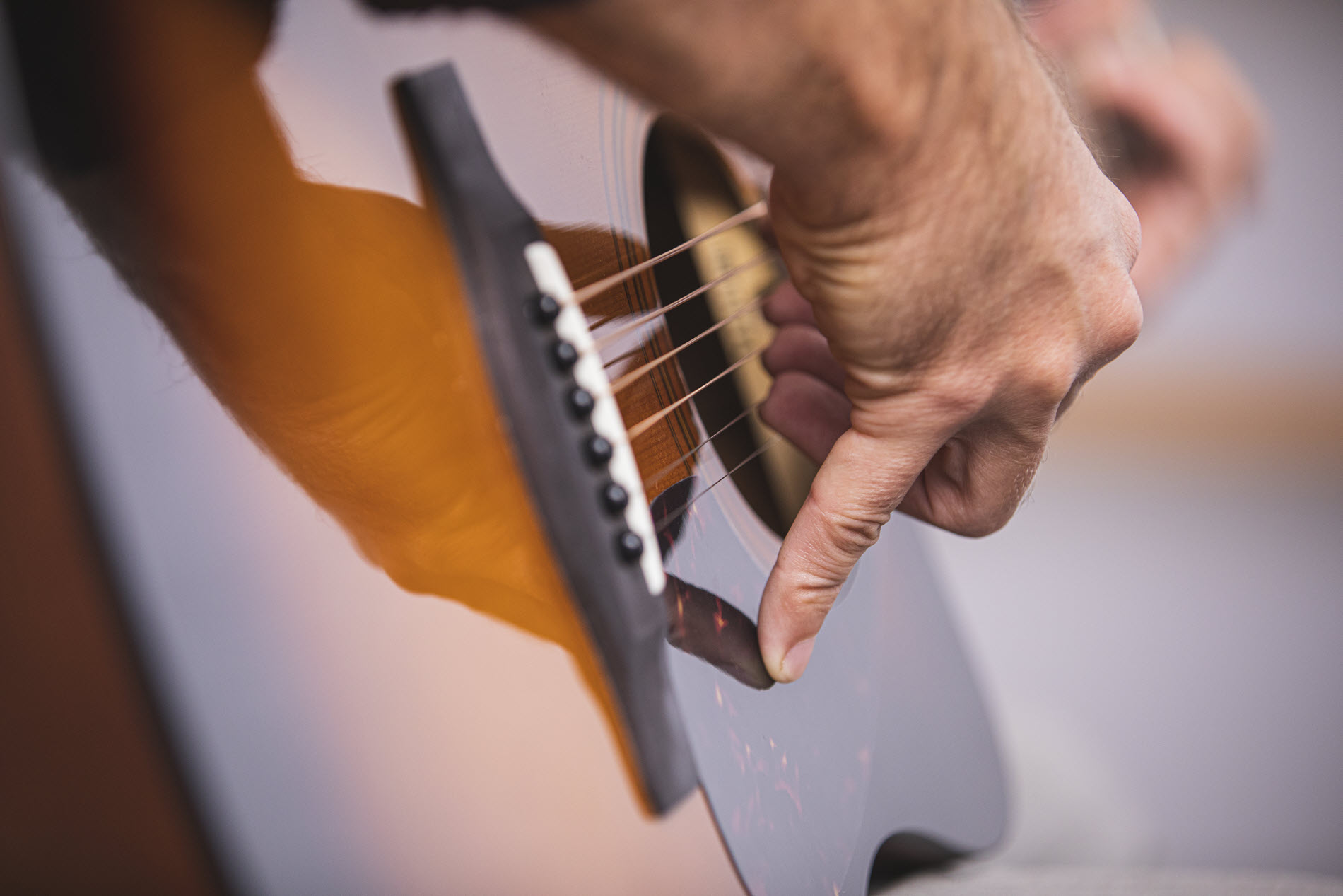 Closeup of someone's hand as they play acoustic guitar.