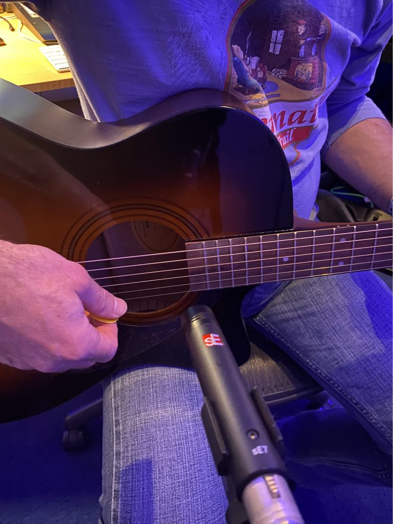 Closeup of someone's hands as they play acoustic guitar with a small directional microphone positioned directly at strings.