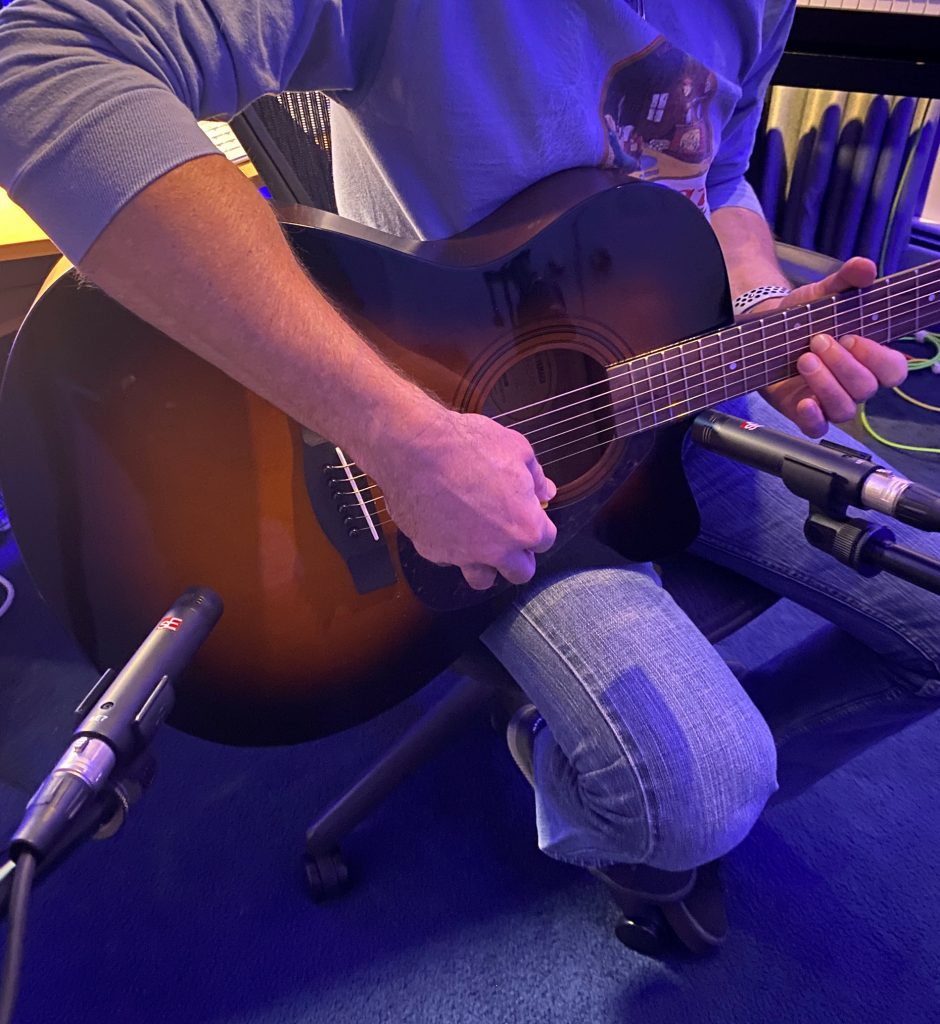 Closeup of someone's hands playing acoustic guitar with microphone positioned at strings.