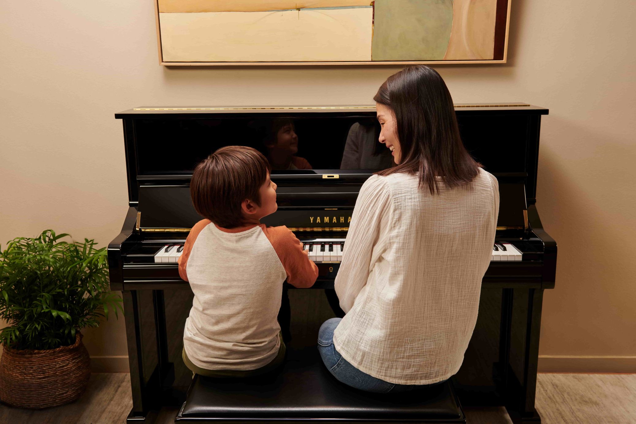 A woman and a boy playing the piano and looking at each other