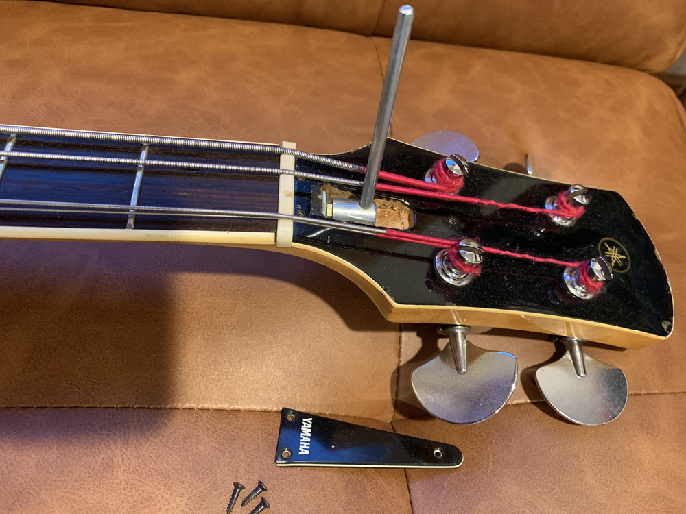 Closeup of bass guitar with allen wrench adjusting the truss rod.