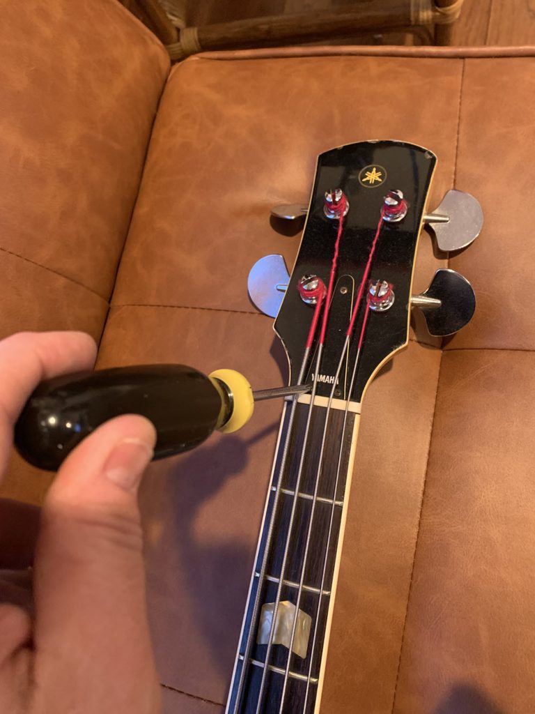 Closeup of someone removing truss cover on bass guitar with screwdriver.
