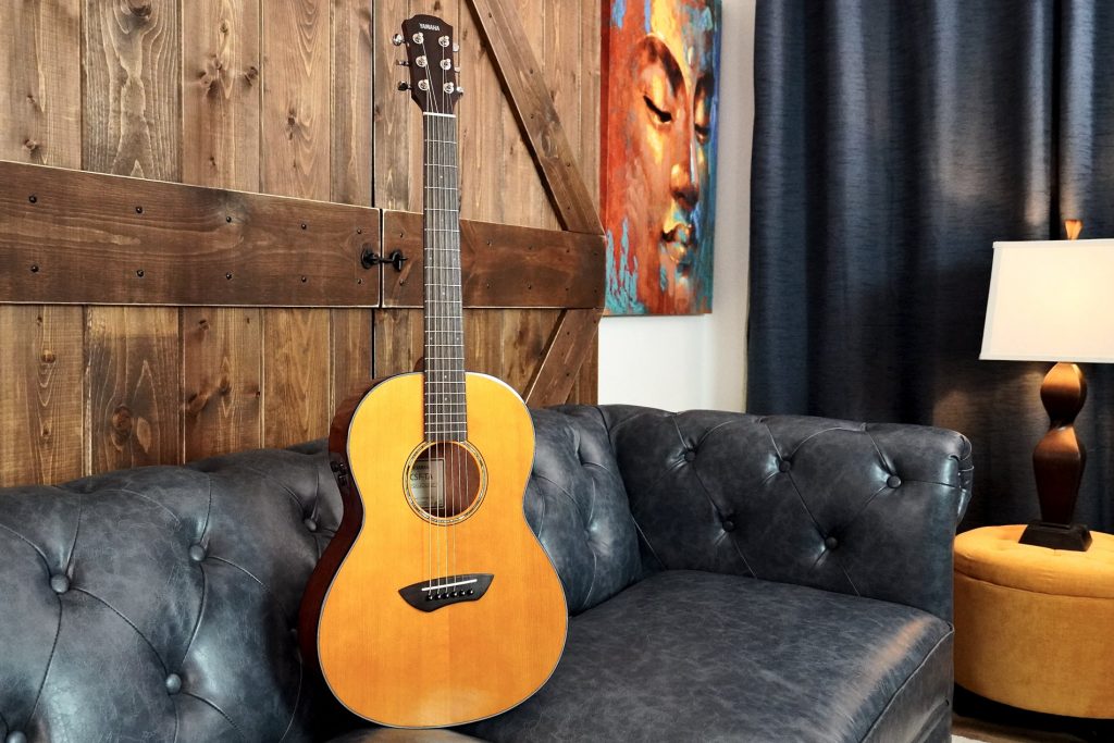 Acoustic guitar propped on leather couch in masculine living room.