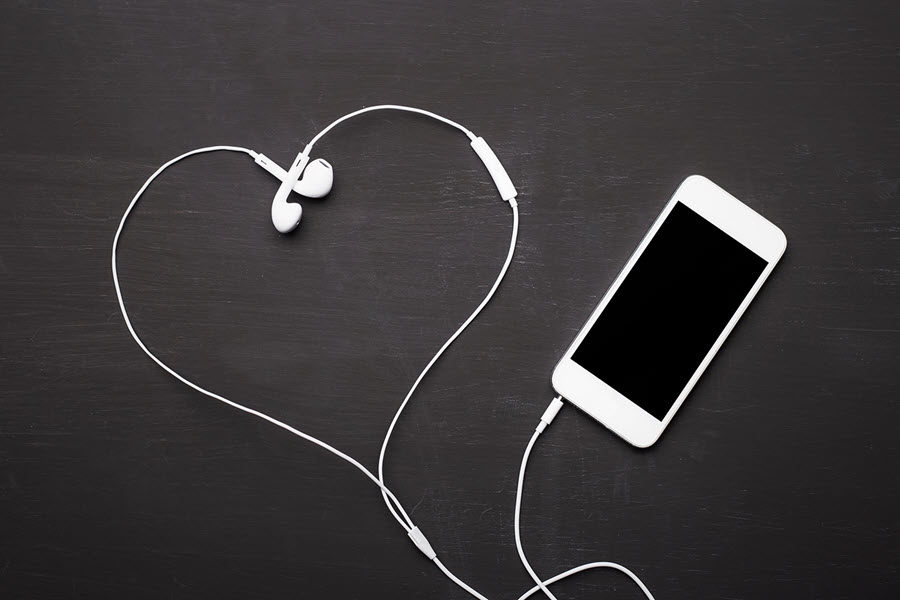 An iphone with wired headphones that have been laid out in a valentine heart shape.