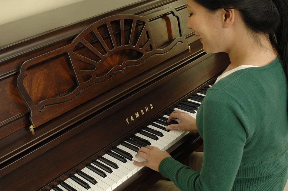 Woman happily playing a Yamaha piano.
