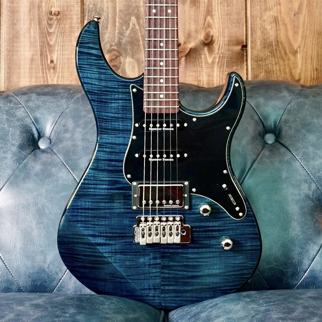 Closeup of body of a blue electric guitar propped up on a blue leather couch.