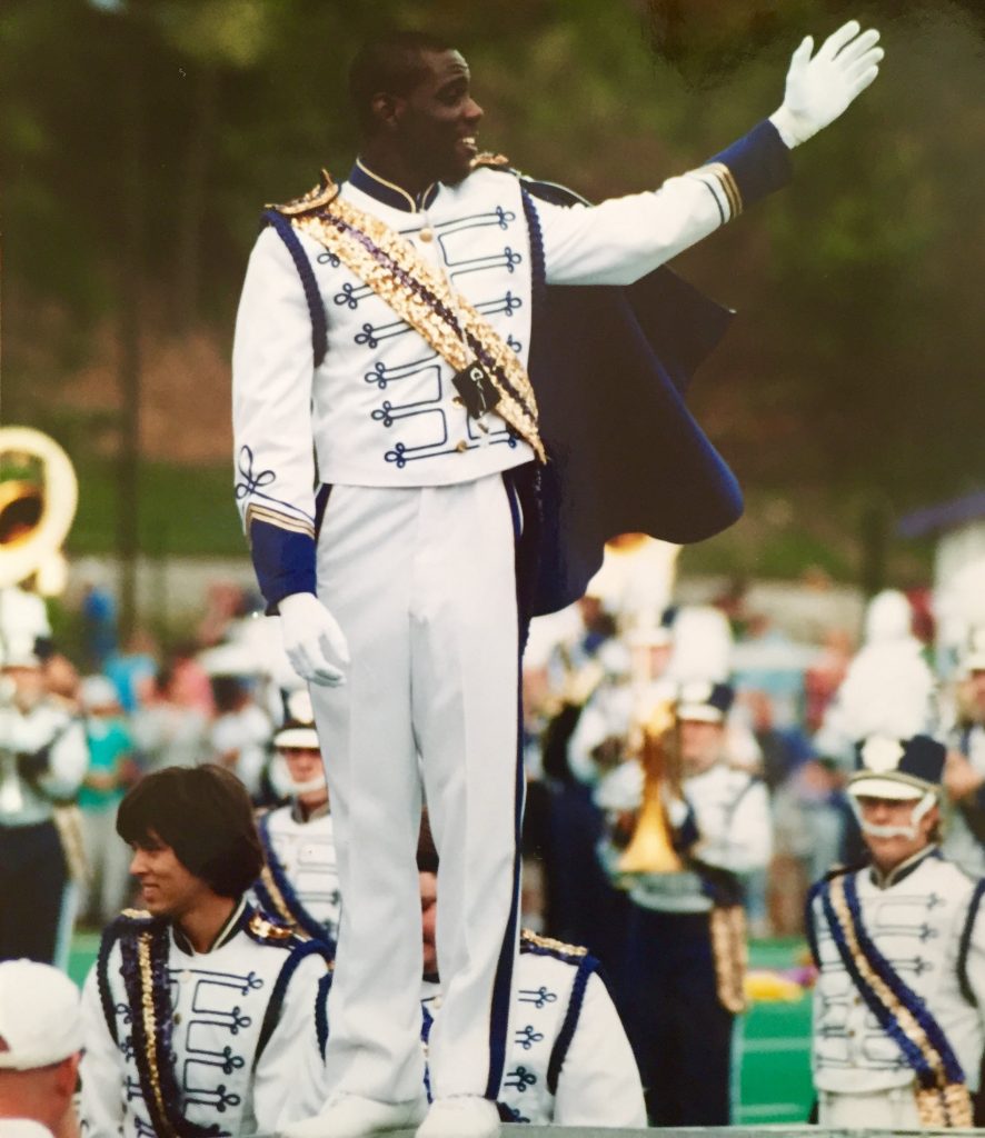 Marching band leader in uniform with his band on field.