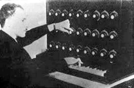 Vintage image of man in suit using the Audion Piano. which look like several rows of dials above a small piano keyboard.