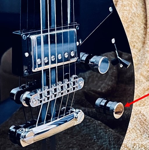 Closeup of the body of an electric guitar with knob indicated.