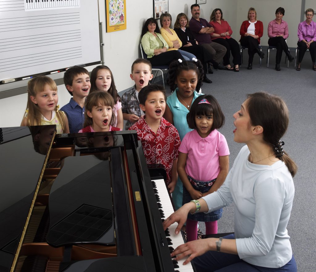teacher playing piano with elementary school students singing