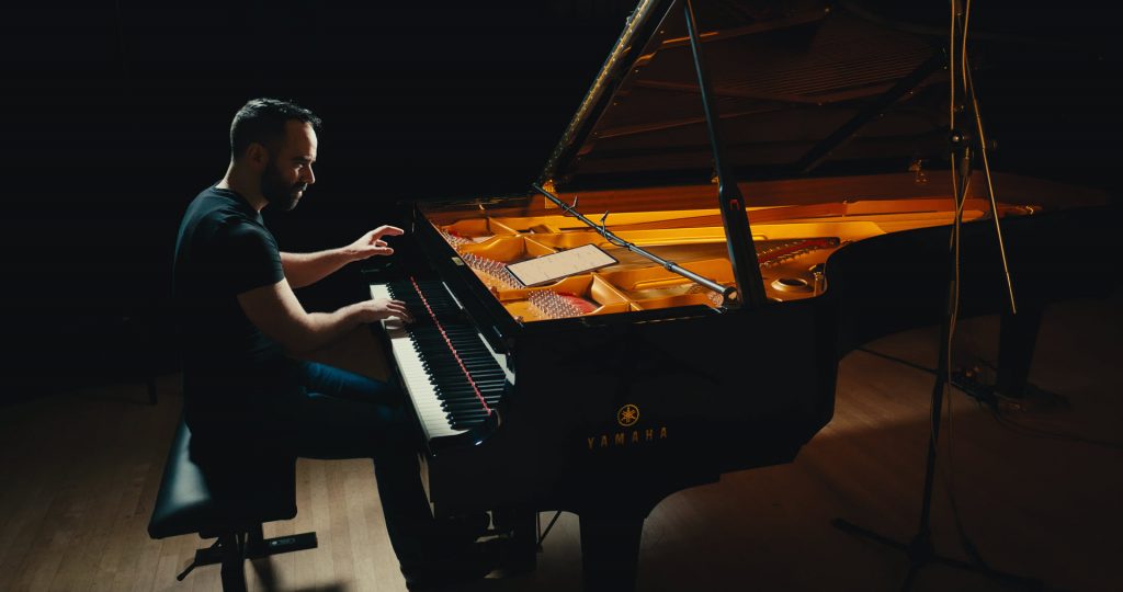 Adam Tendler playing a Yamaha grand piano on a darkened stage.