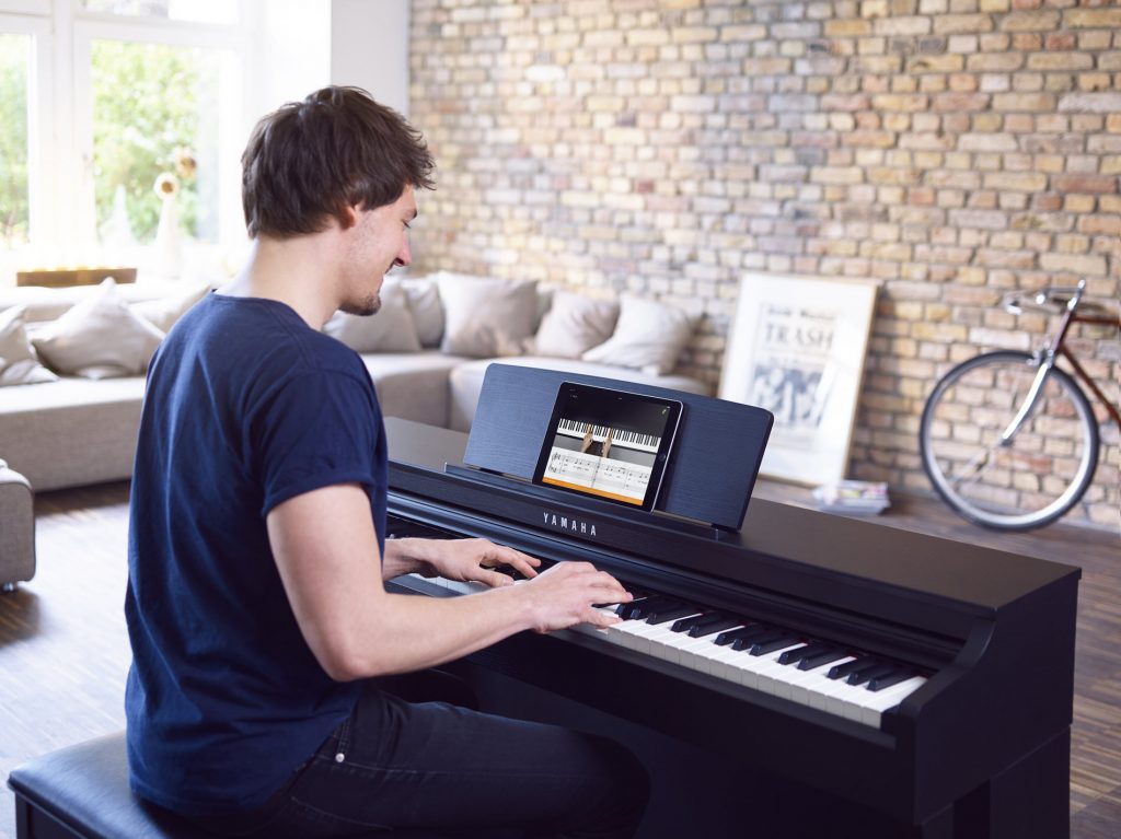 Man playing a small piano with a tablet in front of him displaying an app.