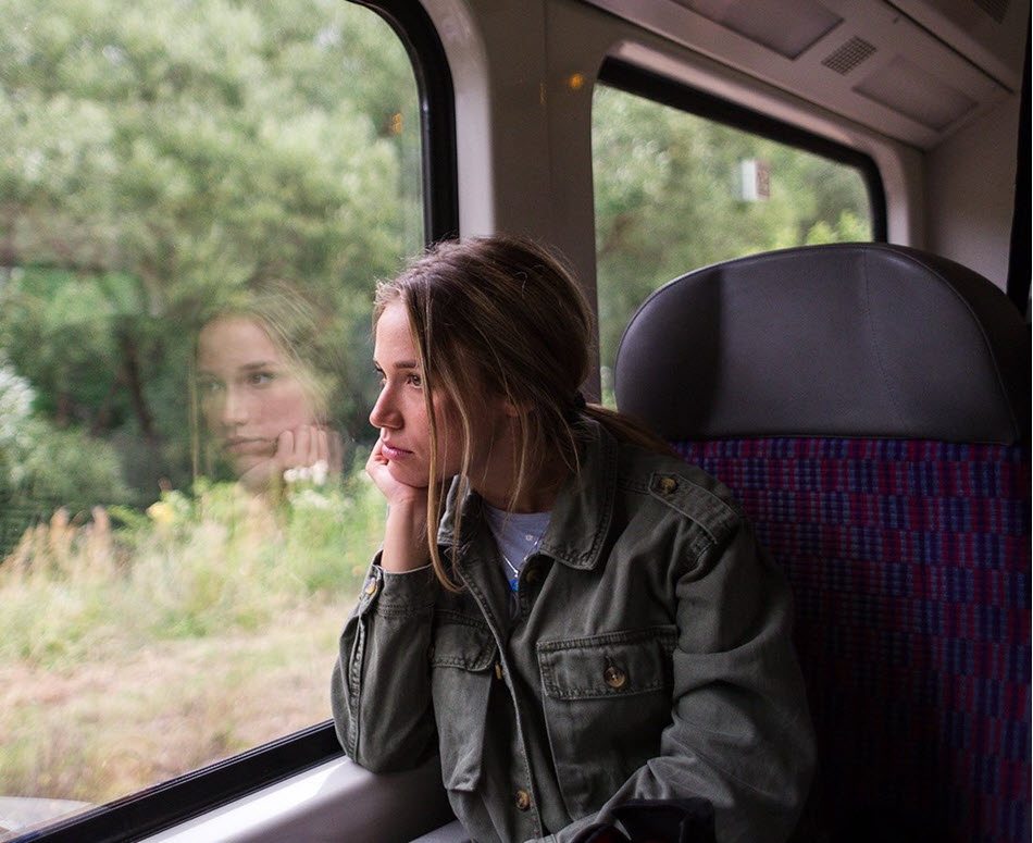 Young woman resting her chin on her hand while looking out a train window.