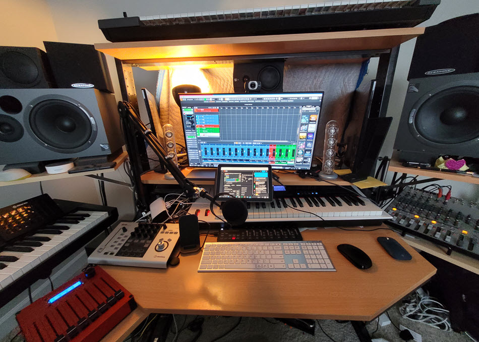 A small studio setup brimming with audio equipment and at center is a computer display with onscreen application.
