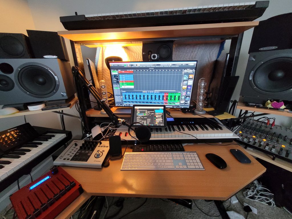 A small studio setup brimming with audio equipment and at center is a computer display with onscreen application.