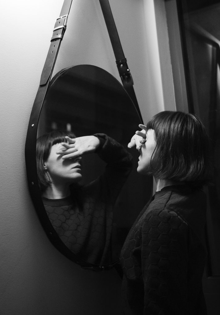 woman with hand over her eyes looking at reflection in mirror