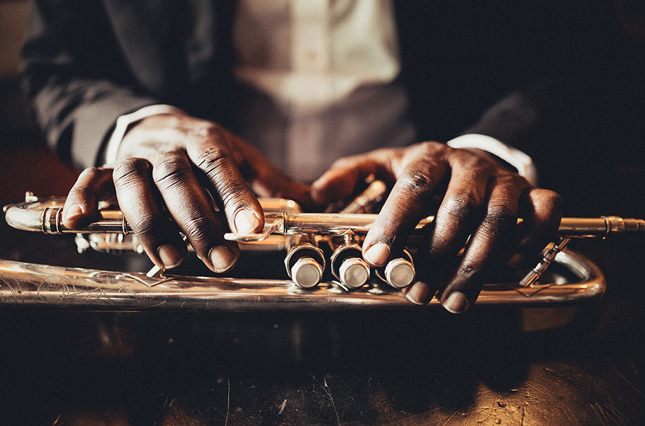 Closeup of a black musician's hands resting on a trumpet on a table.
