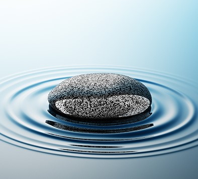 A small stone that has been dropped into a pool of water. There are concentric ripples emanating out from the rock in the water.