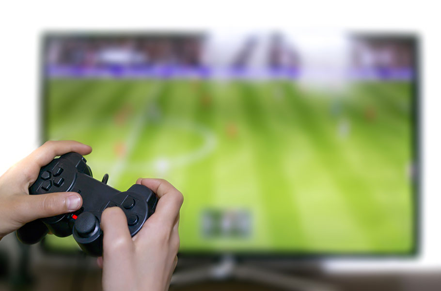 Closeup of someone's hands using a gaming controller with game onscreen in background.