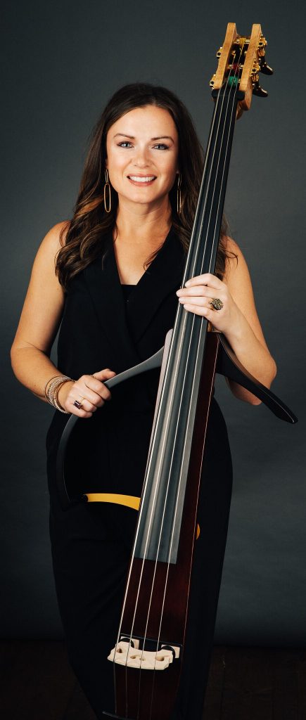 Woman in black dress with an upright electronic bass instrument posed for formal photo.