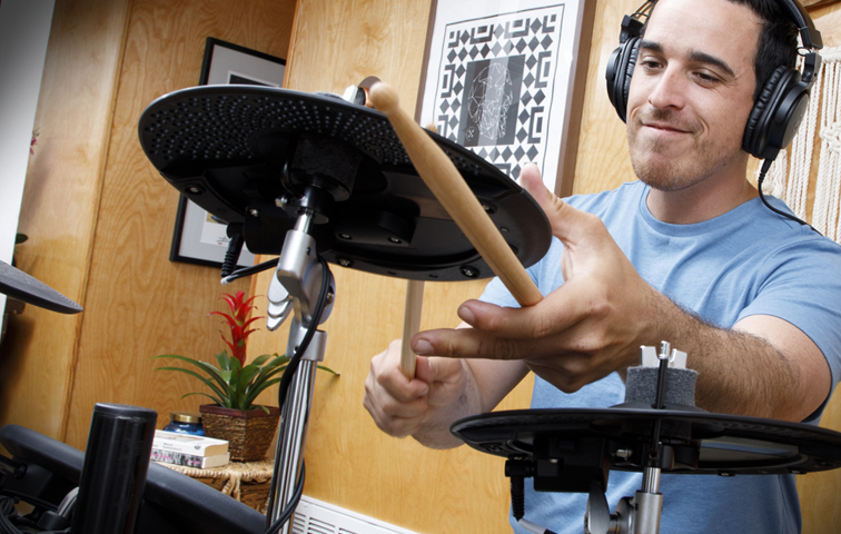 Guy wearing headphones happily playing an electronic drum kit.
