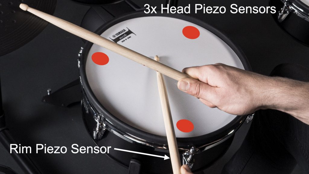 Image of drum and someone playing with drumsticks. There are red spots on the drum head indicating where are the 3 sensors.