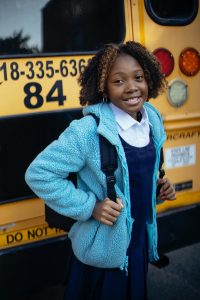 happy girl standing by school bus